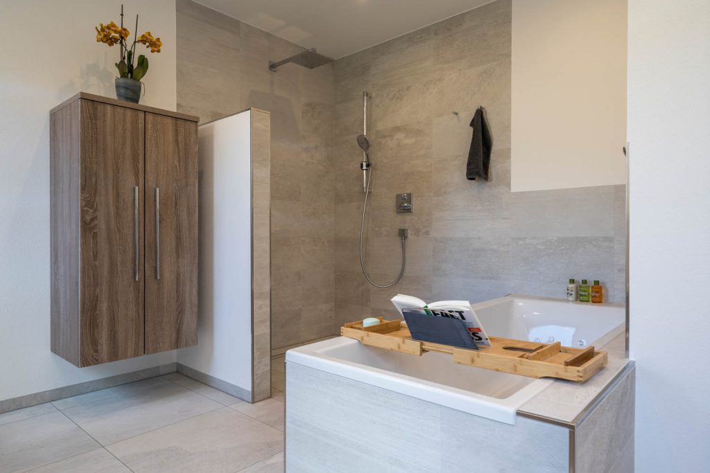 Bodengleiche Dusche hinter halbhoher Trennwand, davor die Badewanne