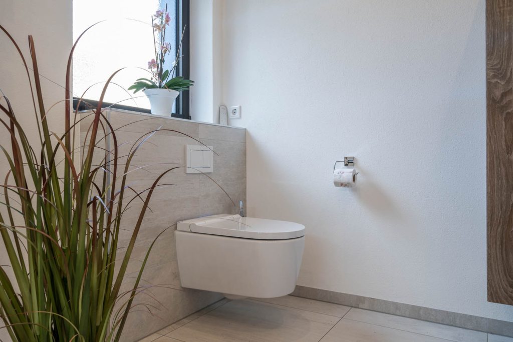 Wand-WC vor gefliester Vorwand unter dem Fenster mit Orchidee