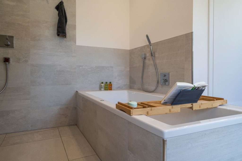 Eingemauerte Wanne mit Holzablage und Buch, Handbrause an der Wand
