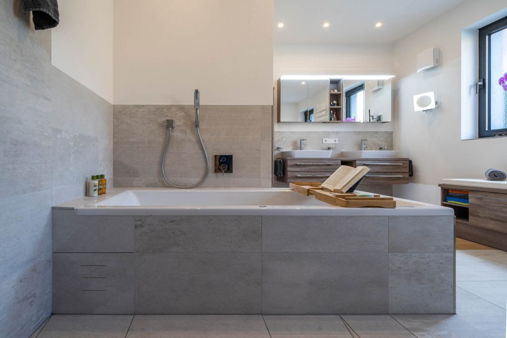 Badewanne mit Holzablage, im Hintergrund Doppelwaschtisch und Fenster