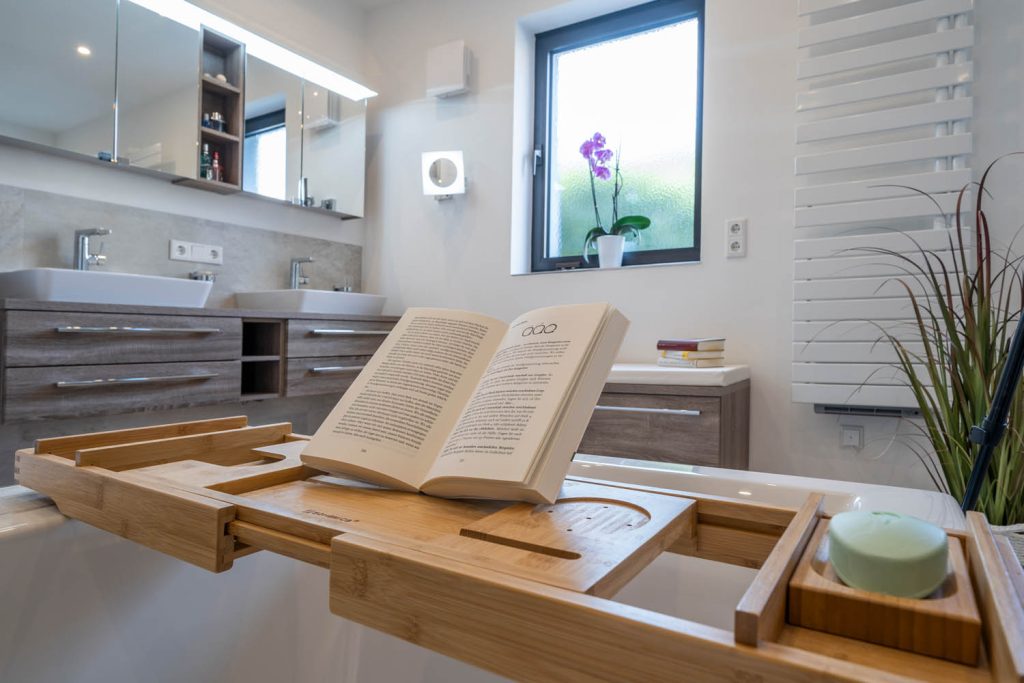Wannenablage mit Buch und Kerze, dahinter Waschtisch und Fenster
