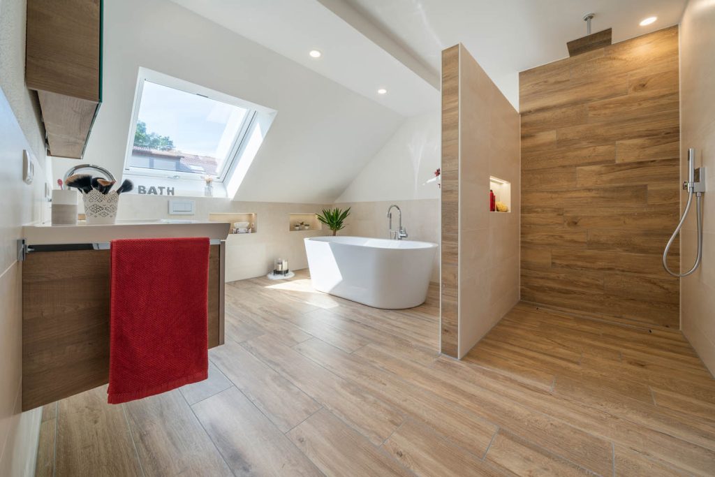 Dachgeschossbad mit Holzoptik-Boden, freistehender Wanne und Dusche hinter einer Trennwand