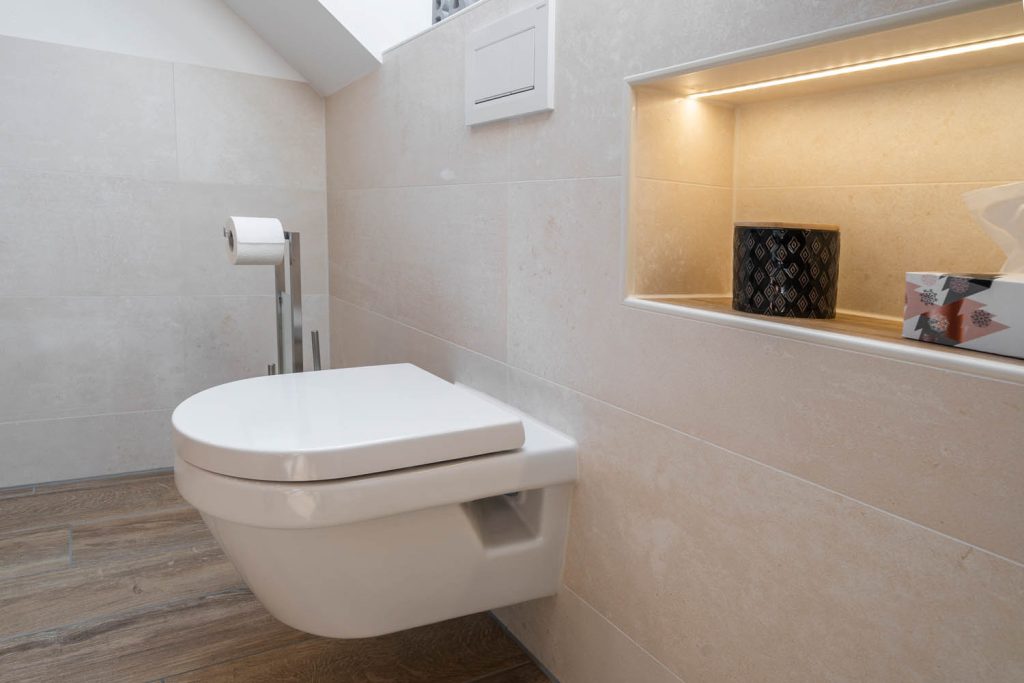 Wand-WC neben einer beleuchteten Wandnische mit Deko