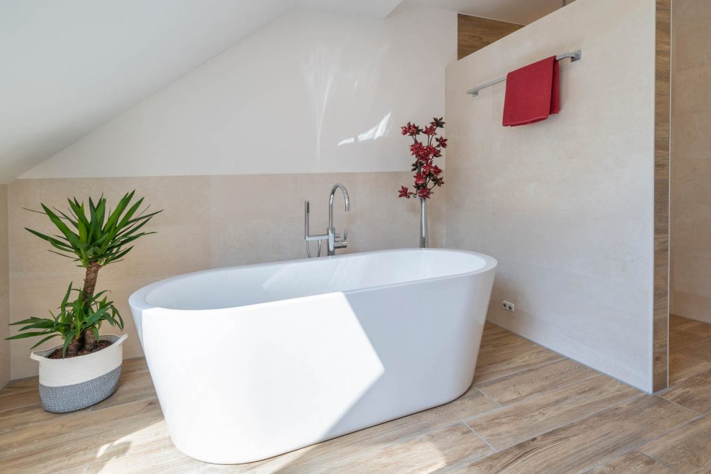 Freistehende Badewanne mit Standarmatur, links Pflanze im Korb