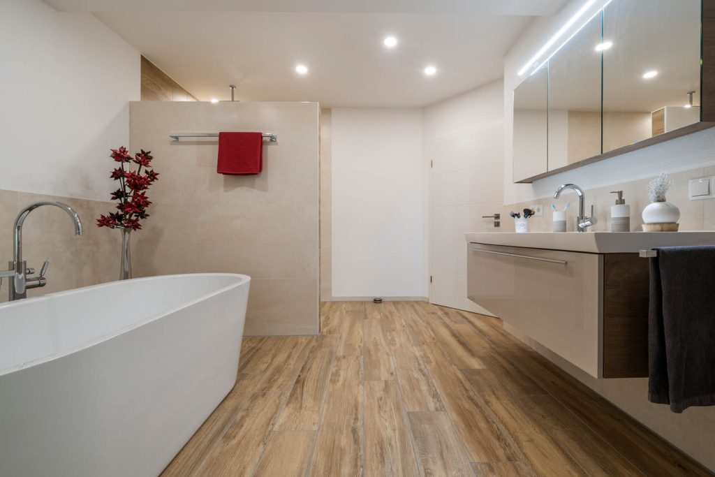 Badewanne im Vordergrund, dahinter Waschtisch mit Lichtspiegel