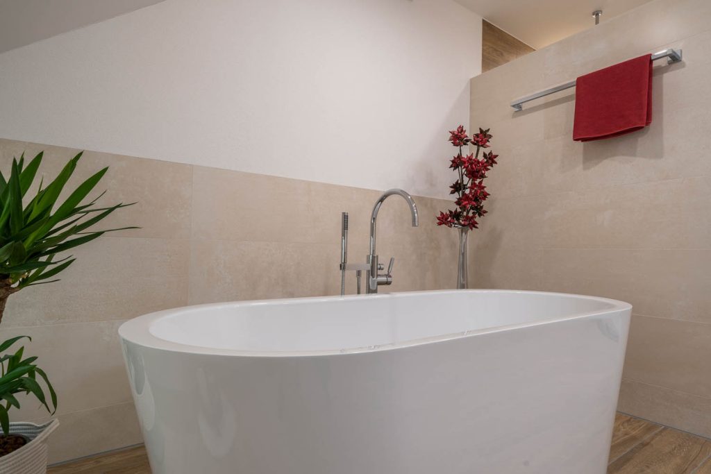 Freistehende Wanne vor der Trennwand mit rotem Handtuch