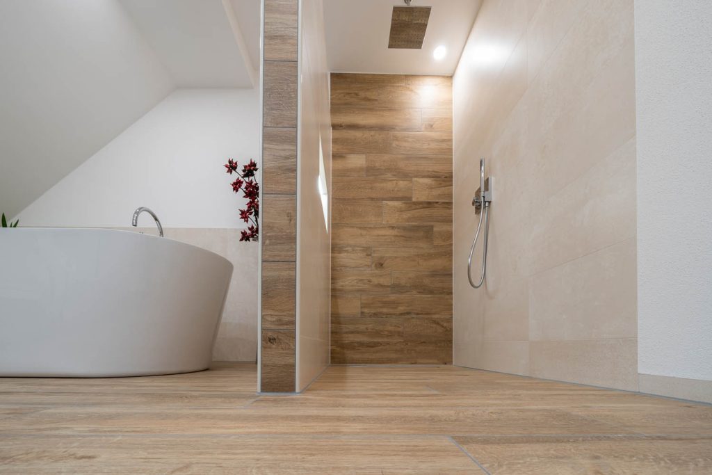 Begehbare Dusche mit Rückwand in Holzoptik, links die Badewanne
