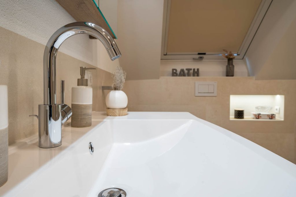 Detail der Waschtischarmatur, im Hintergrund WC und beleuchtete Nische