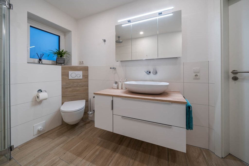 Wand-WC vor Vorwand in Holzoptik, daneben Waschtisch mit Spiegelschrank
