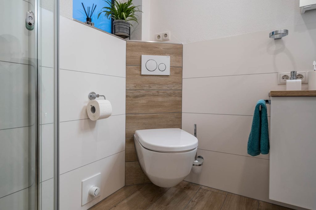 Wand-WC vor holzfarbener Vorwand, rechts der weiße Waschtisch