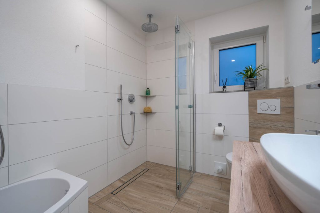 Dusche mit geöffneter Glastür, links Wanne, rechts Waschtisch