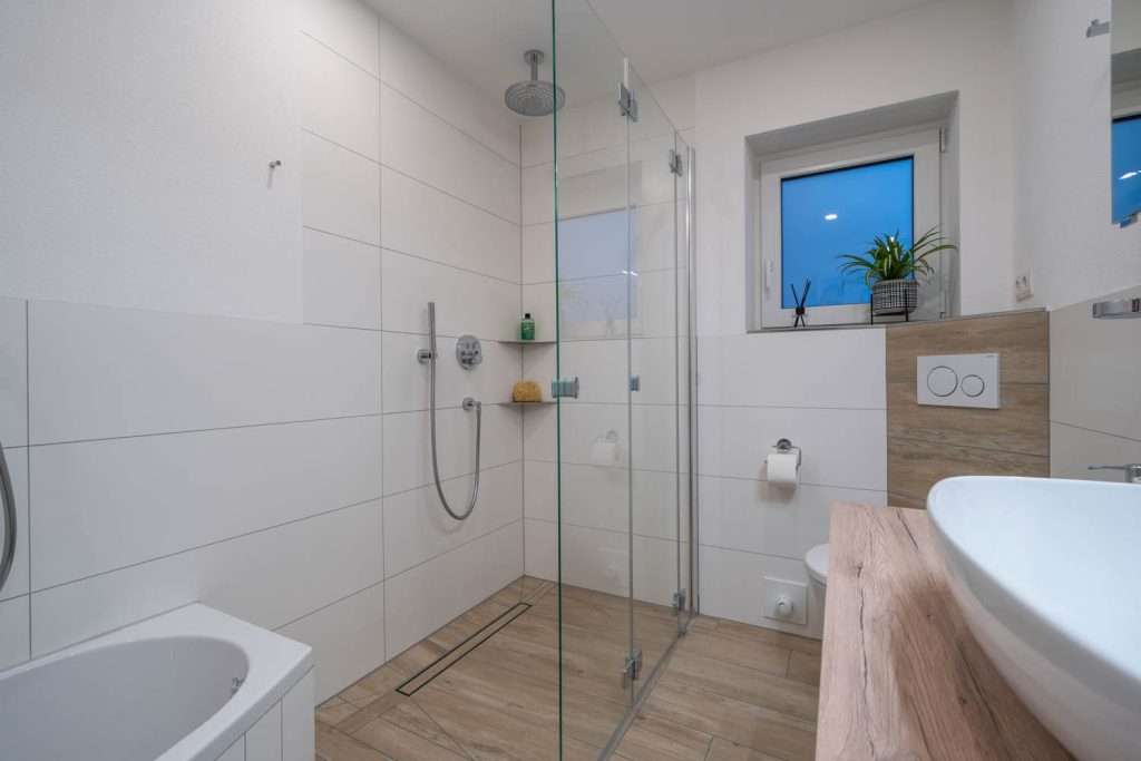 Glasdusche mit Duschrinne und Eckablagen neben dem WC