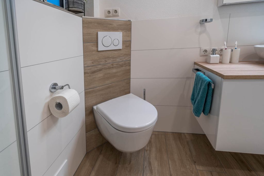 Wand-WC mit Papierhalter, daneben Waschtisch mit türkisem Handtuch