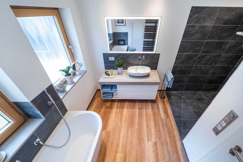 Blick über die Wanne zum Waschtisch und zur dunklen Duschwand