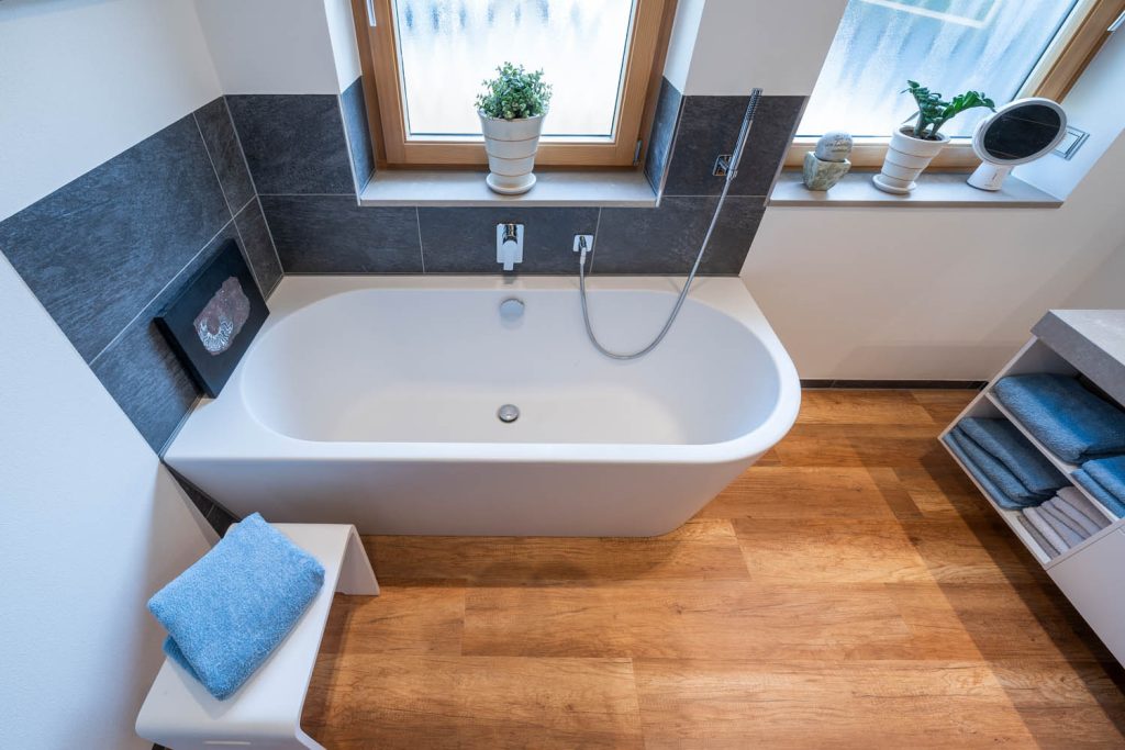 Badewanne unter dem Fenster mit Holzboden, rechts offene Handtuchfächer