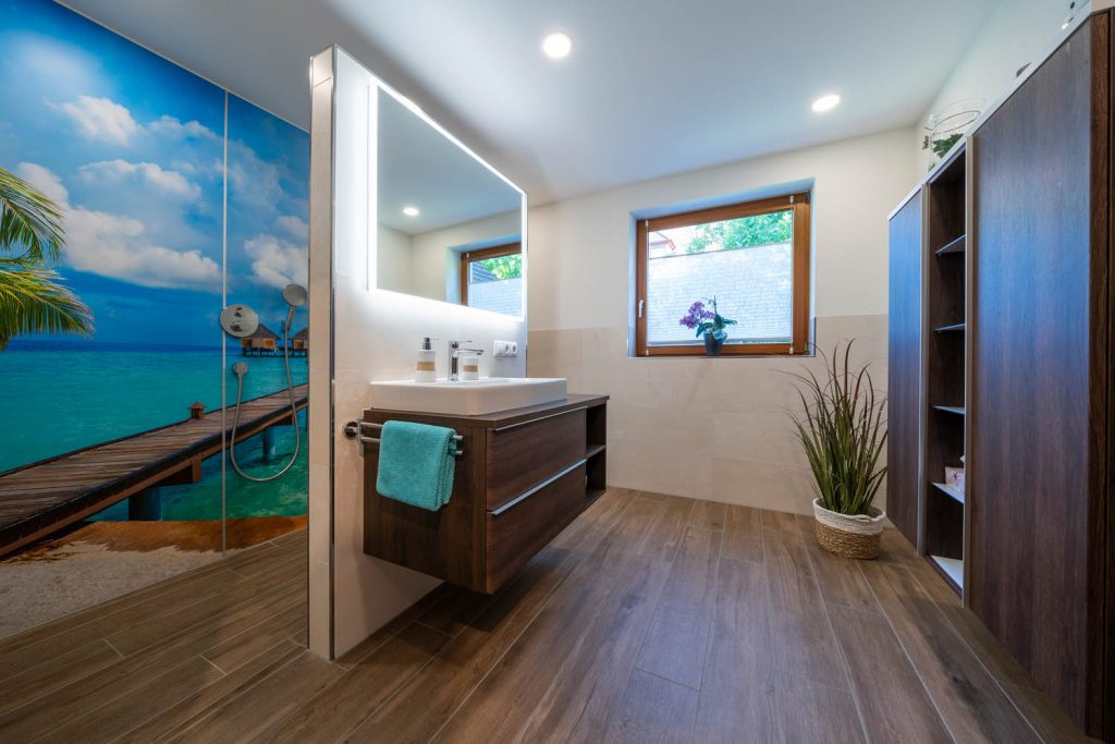 Waschtisch vor einer Trennwand, links die Dusche mit tropischem Wandmotiv