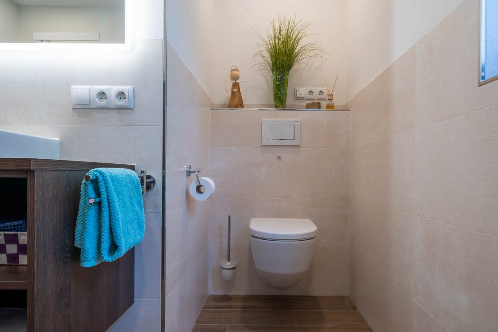 Wand-WC hinter der Trennwand vor hellen Fliesen mit Ablage