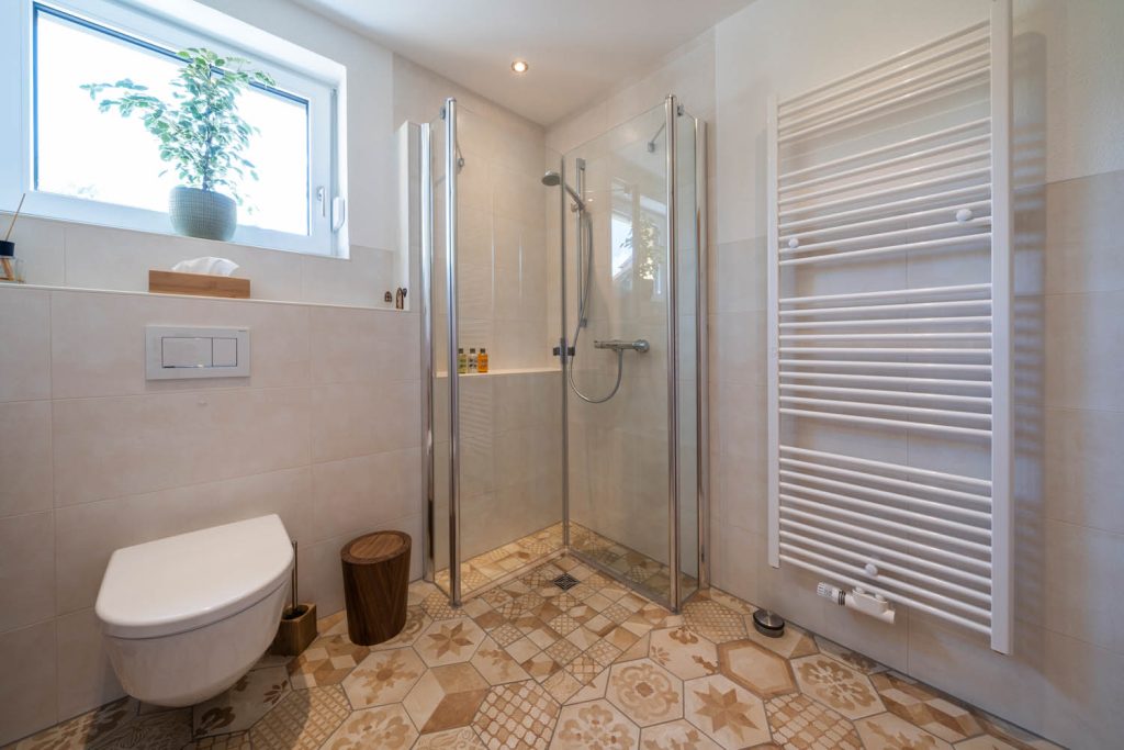 Eckdusche mit Glastüren neben dem Wand-WC, rechts Handtuchheizkörper