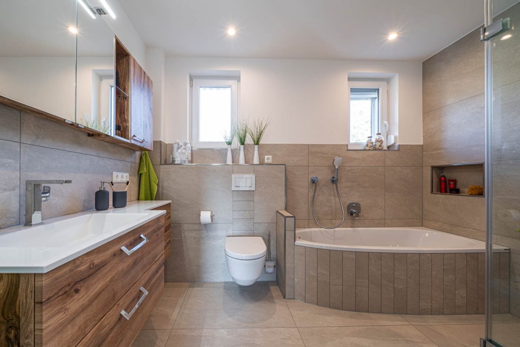 Langer Waschtisch mit Holzfront, dahinter Wand-WC und Eckbadewanne
