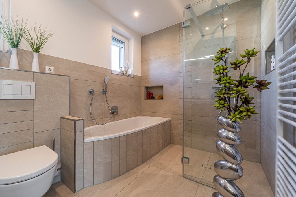 Eckbadewanne mit Fliesenschürze neben der Glasdusche