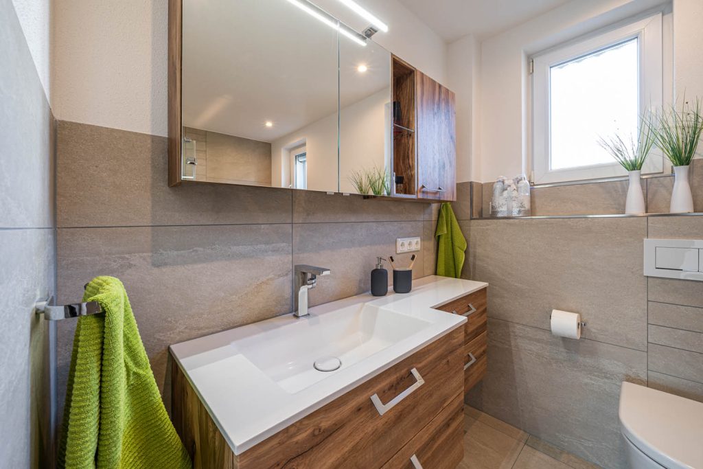 Waschtisch mit grünem Handtuch und Spiegelschrank mit Holzfach
