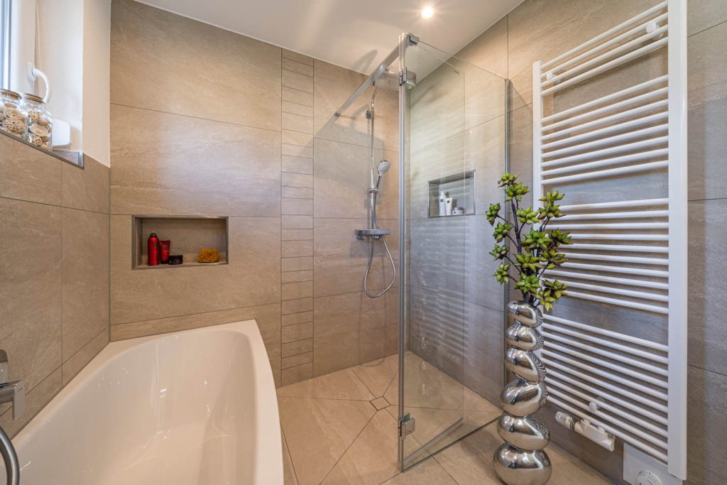 Eckdusche mit Glaswänden und Wandnische, links die Wanne