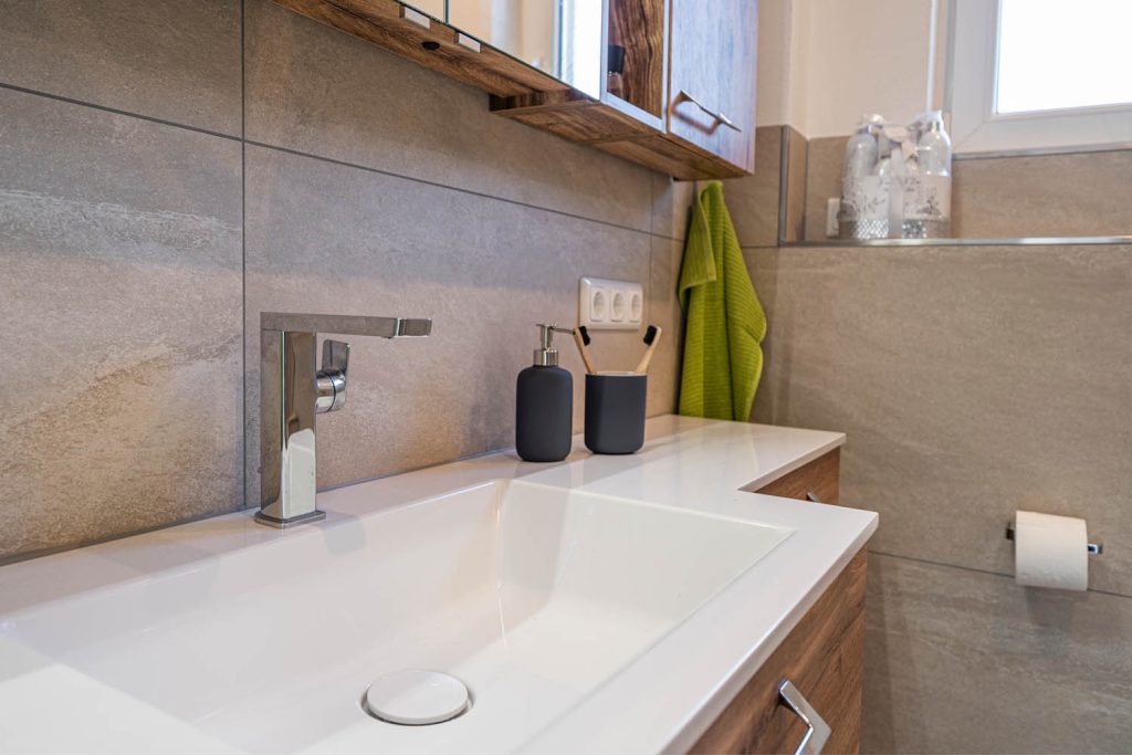 Waschbecken mit Armatur und Accessoires vor Fliesen in Greige