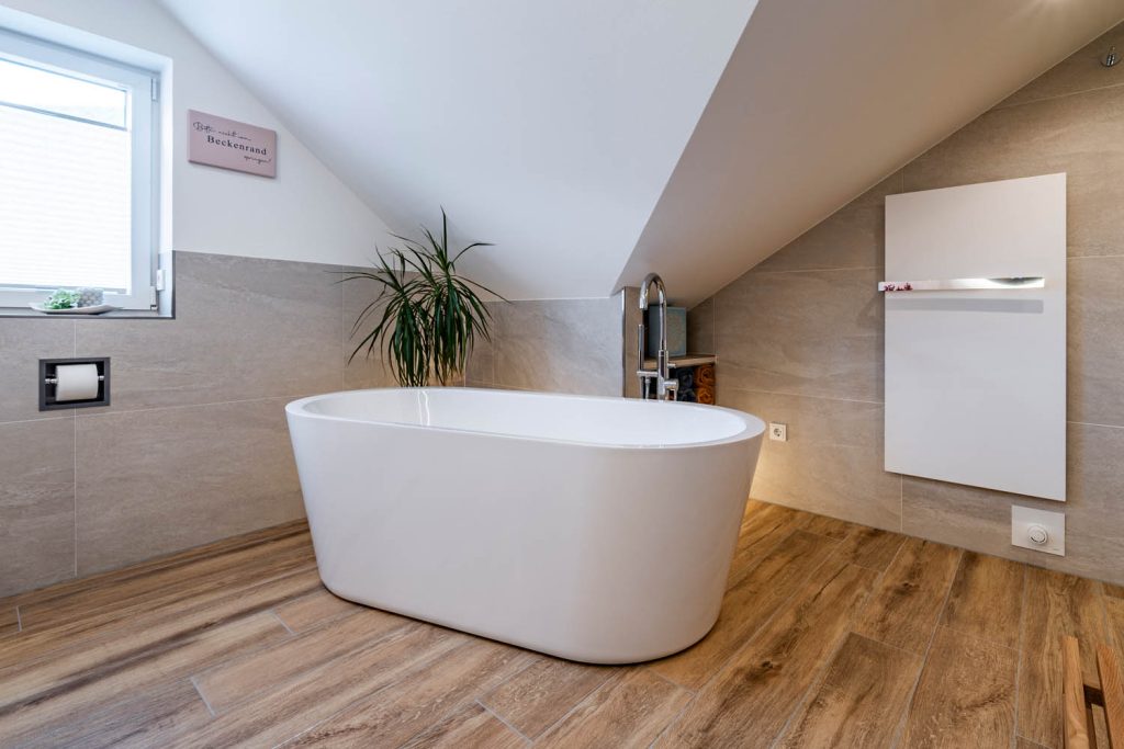 Freistehende Badewanne vor beleuchtetem Regal und Heizkörper