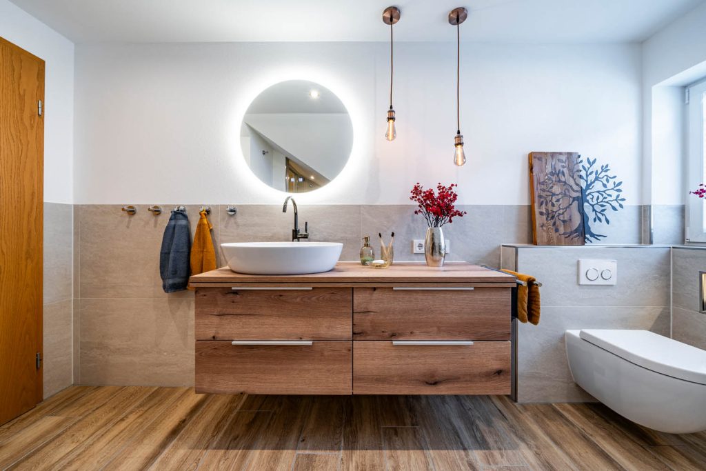 Waschtisch in Holzoptik mit rundem Lichtspiegel, Pendelleuchten und Wand-WC