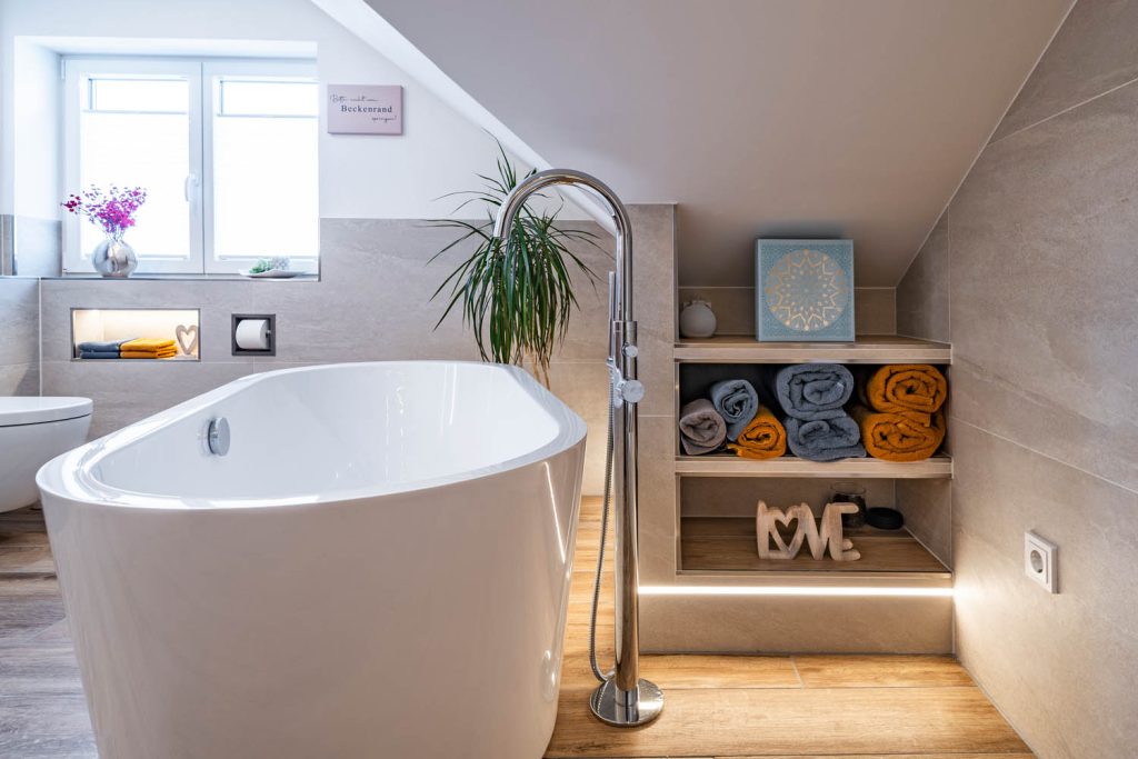 Wanne vor einem Einbauregal mit bunten Handtüchern und Lichtleiste