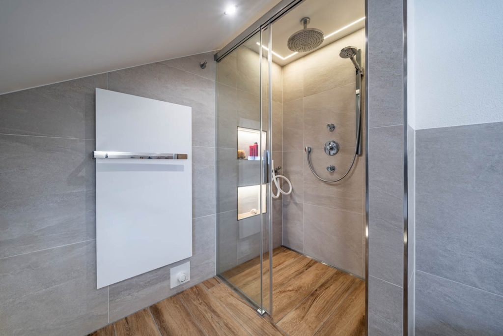 Dusche mit Glasschiebetür und beleuchteten Nischen, links Flächenheizkörper