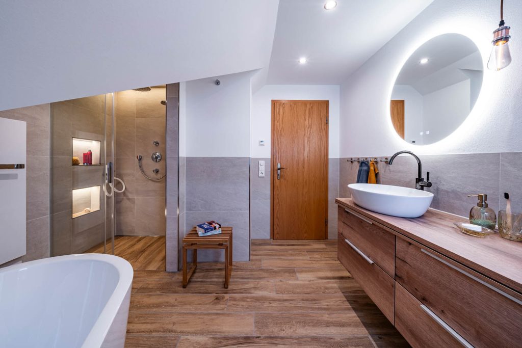 Blick zur Dusche und Holztür, rechts Waschtisch mit rundem Spiegel
