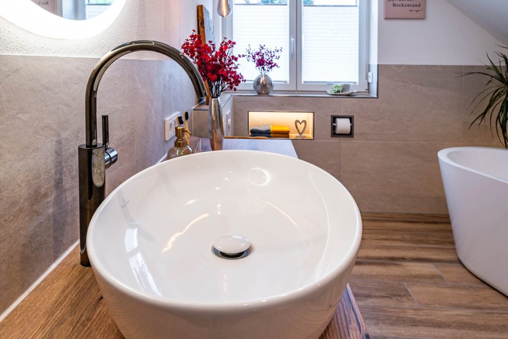 Ovales Aufsatzbecken mit Armatur, im Hintergrund WC und Wanne