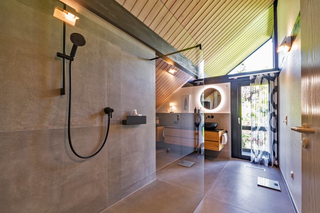 Dachbad mit Holzdecke, bodengleicher Dusche in Betonoptik und Waschtisch mit rundem Lichtspiegel