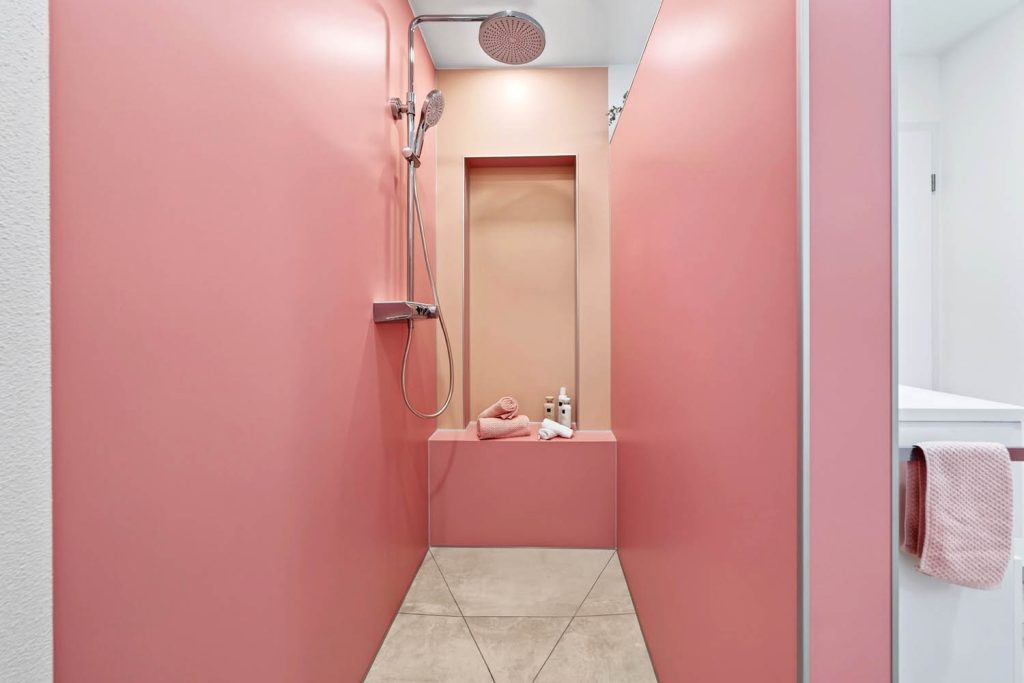 Begehbare Dusche mit rosé Wänden, Kopfbrause und Sitzbank vor einer apricotfarbenen Nische