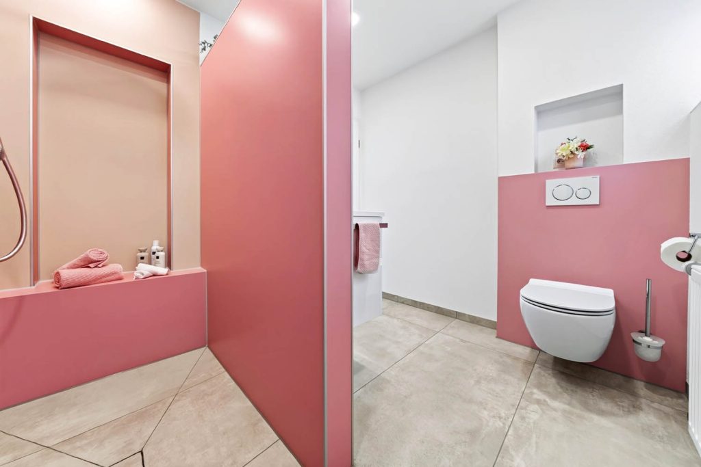 Blick von der Dusche mit Sitzbank hinüber zum Wand-WC vor rosé Vorwand