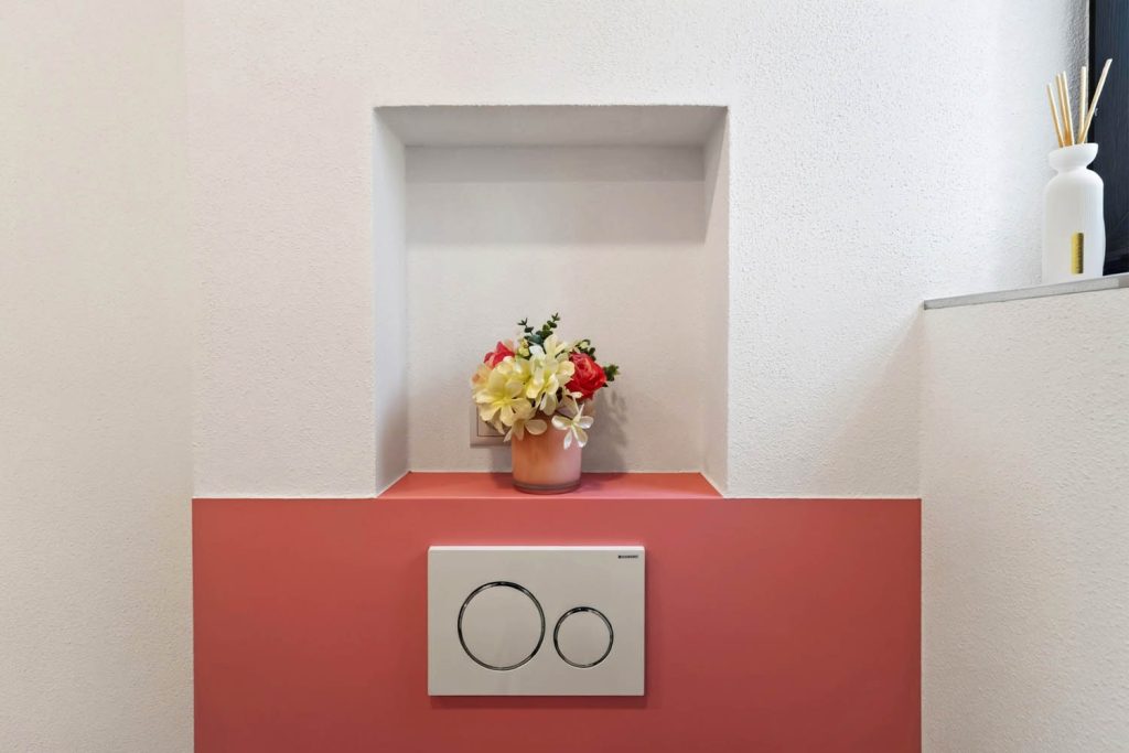 Ablagenische mit Blumenstrauß über der rosé Vorwand mit weißer Drückerplatte
