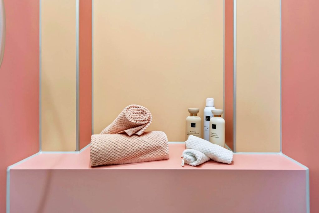 Sitzbank in der Dusche mit gerollten Handtüchern und Pflegeprodukten vor apricotfarbener Nische