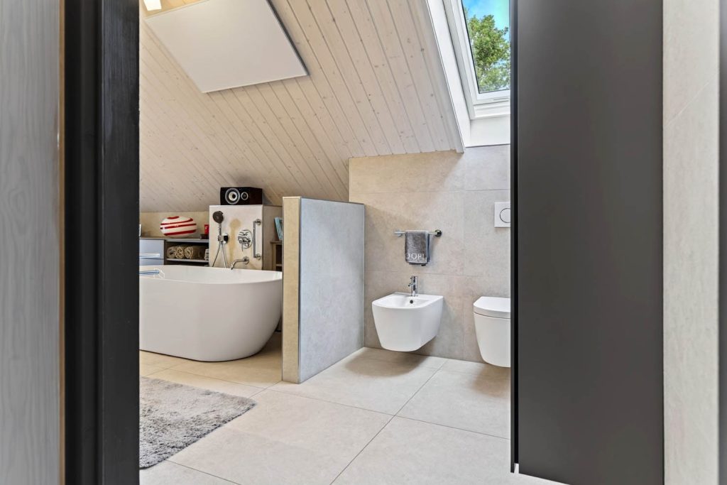 Blick durch die Tür ins Dachgeschossbad mit freistehender Badewanne, Trennwand und Wand-WC