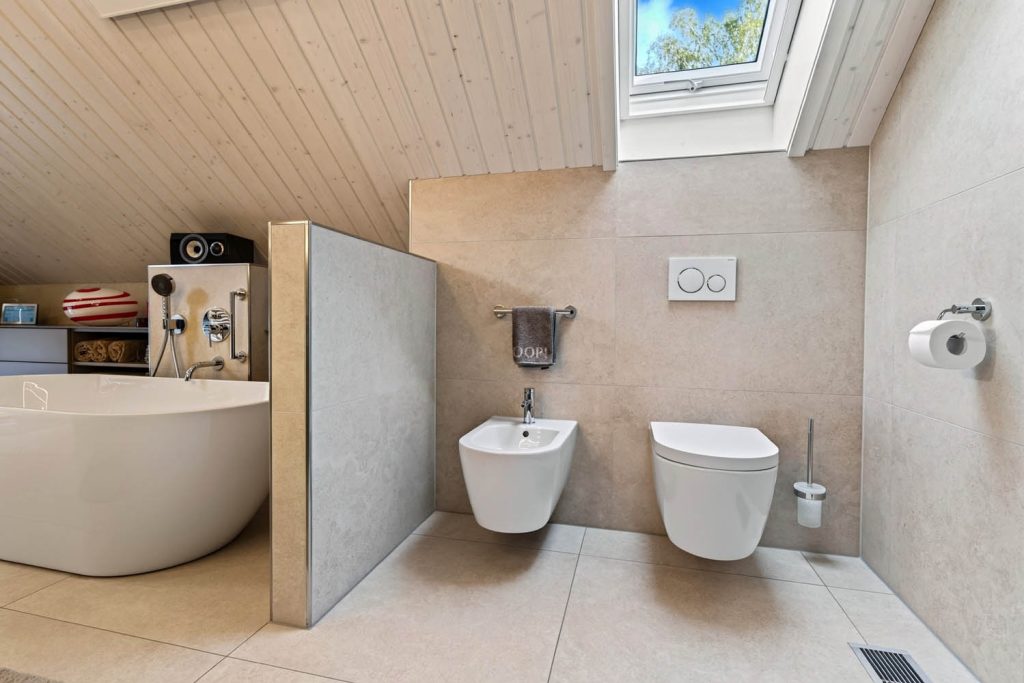 Freistehende Wanne hinter einer halbhohen Trennwand, daneben Bidet und WC unter der Dachschräge