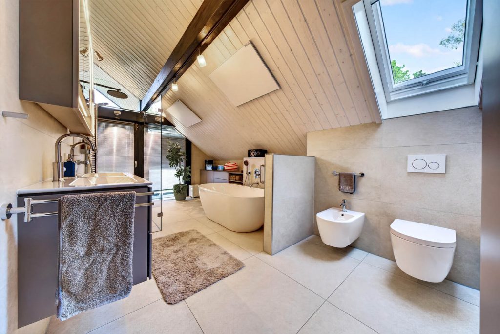 Waschtisch mit grauem Unterschrank im Vordergrund, dahinter Wanne, Bidet und WC
