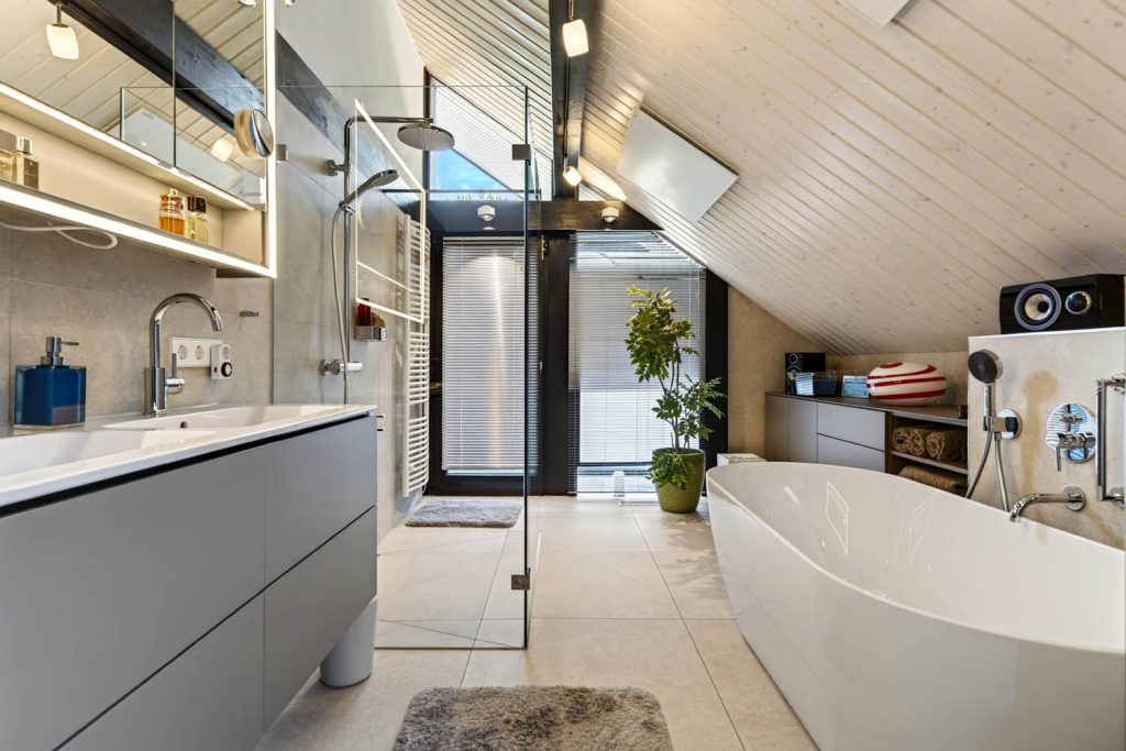 Waschtisch und freistehende Wanne unter der weißen Holzdecke, im Hintergrund Glastür ins Freie