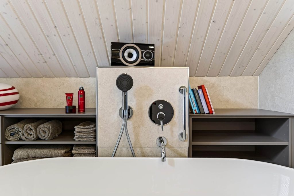 Blick über den Wannenrand auf Vorwand mit Armatur, seitlich offene Regale mit Handtüchern
