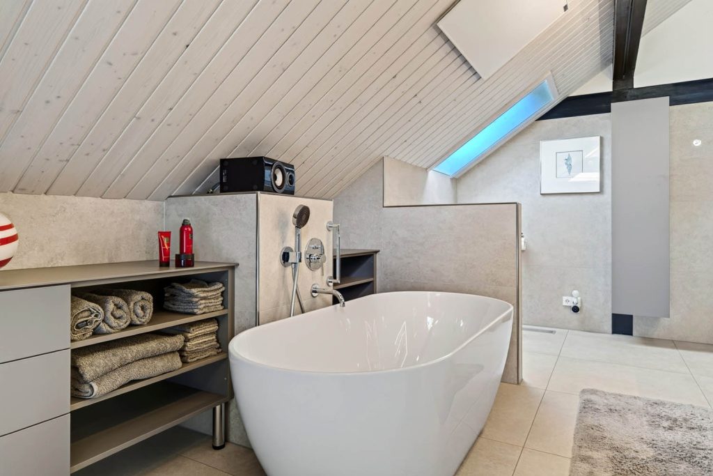 Freistehende Wanne vor halbhoher Vorwand, daneben Sideboard mit gerollten Handtüchern