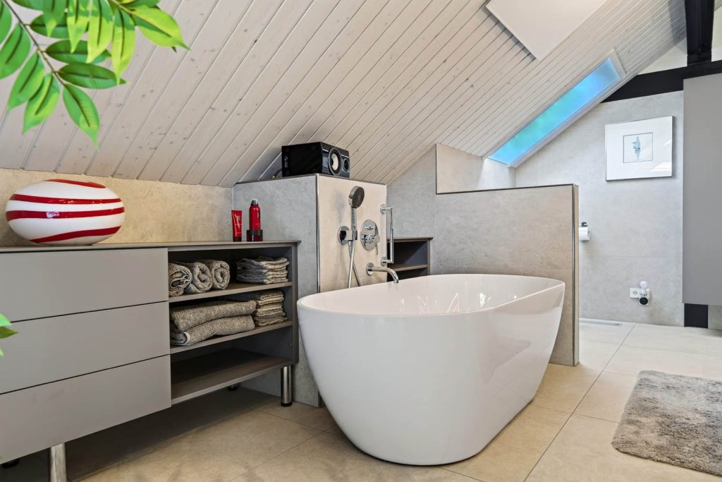 Badewanne vor Sideboard und Regal, im Hintergrund Wandbild und Dachfenster