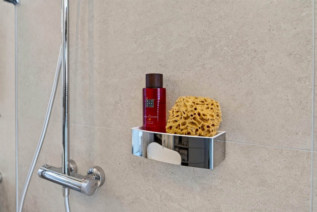 Thermostat und Ablage mit Duschgel und Schwamm an der gefliesten Duschwand