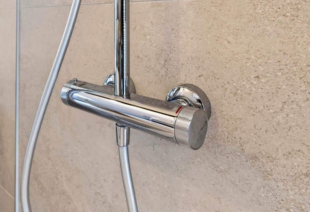 Detail des verchromten Brausethermostats an der Duschwand in Steinoptik