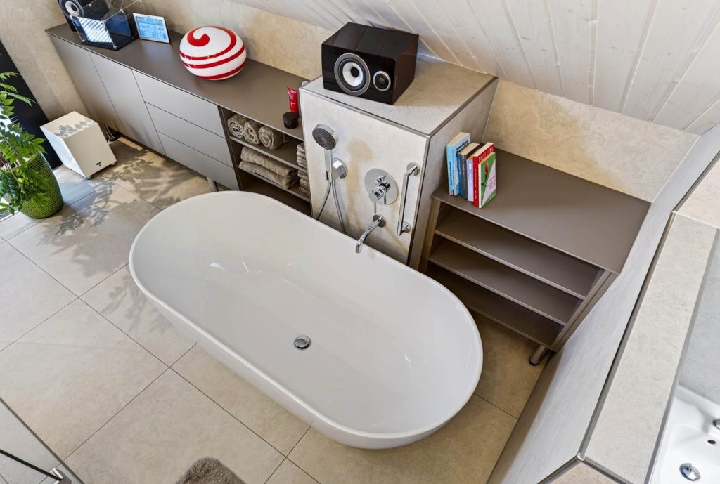 Ovale Badewanne von oben, dahinter Regale mit Handtüchern und Deko