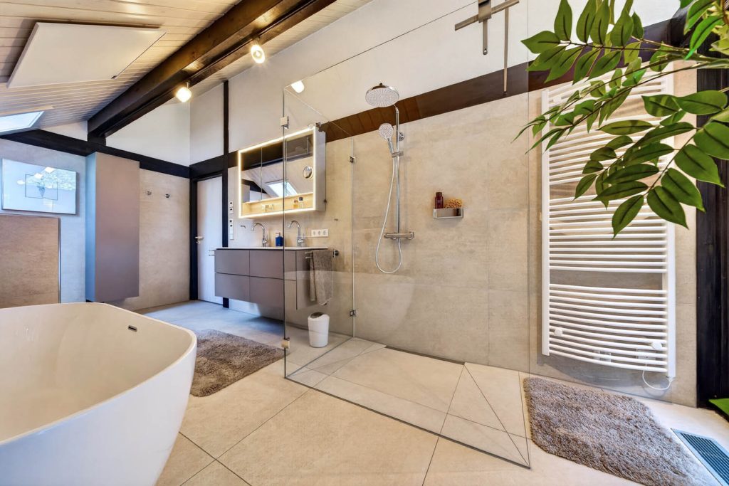 Raumansicht mit Wanne im Vordergrund, Glasdusche und Waschtisch unter dem Dachbalken