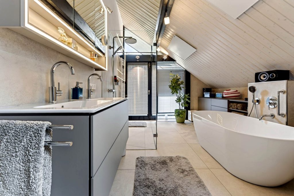 Waschtisch mit Handtuch im Vordergrund, dahinter Dusche und freistehende Badewanne